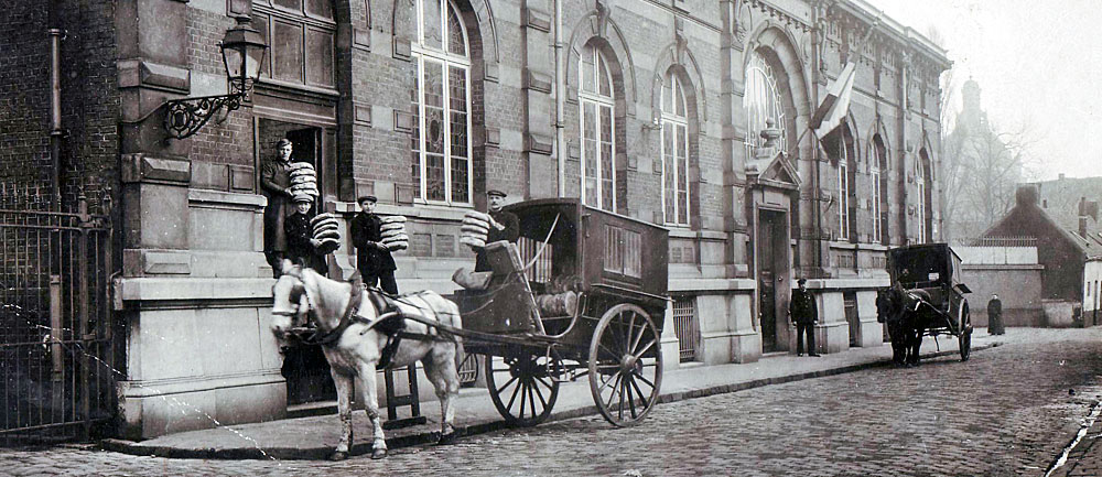 <p>Une charette hippotractée stationne devant la porte de service. Quatre hommes déchargent des pains ronds pour le Bureau.</p>